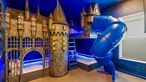 Une pièce décorée sur le thème d’un château, avec un grand fauteuil bleu et une fenêtre équipée de stores.