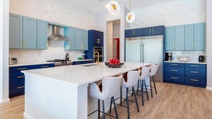 A modern kitchen with a central island, blue cabinets, stainless steel appliances, and pendant lighting.