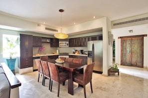 A modern kitchen with dark cabinetry, a stainless steel refrigerator, and a dining area with a wooden table and chairs.