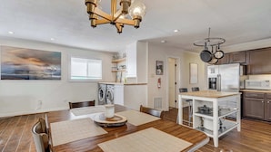 Une cuisine moderne avec un plancher en bois, un coin repas avec une table et des chaises en bois, un four encastré et un réfrigérateur.