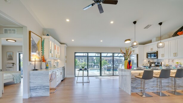 Una cocina moderna con armarios blancos, una isla de mármol y una zona de comedor con taburetes de bar.