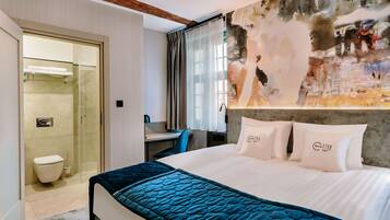 A modern hotel room with a large bed, a desk, and a shower area.
