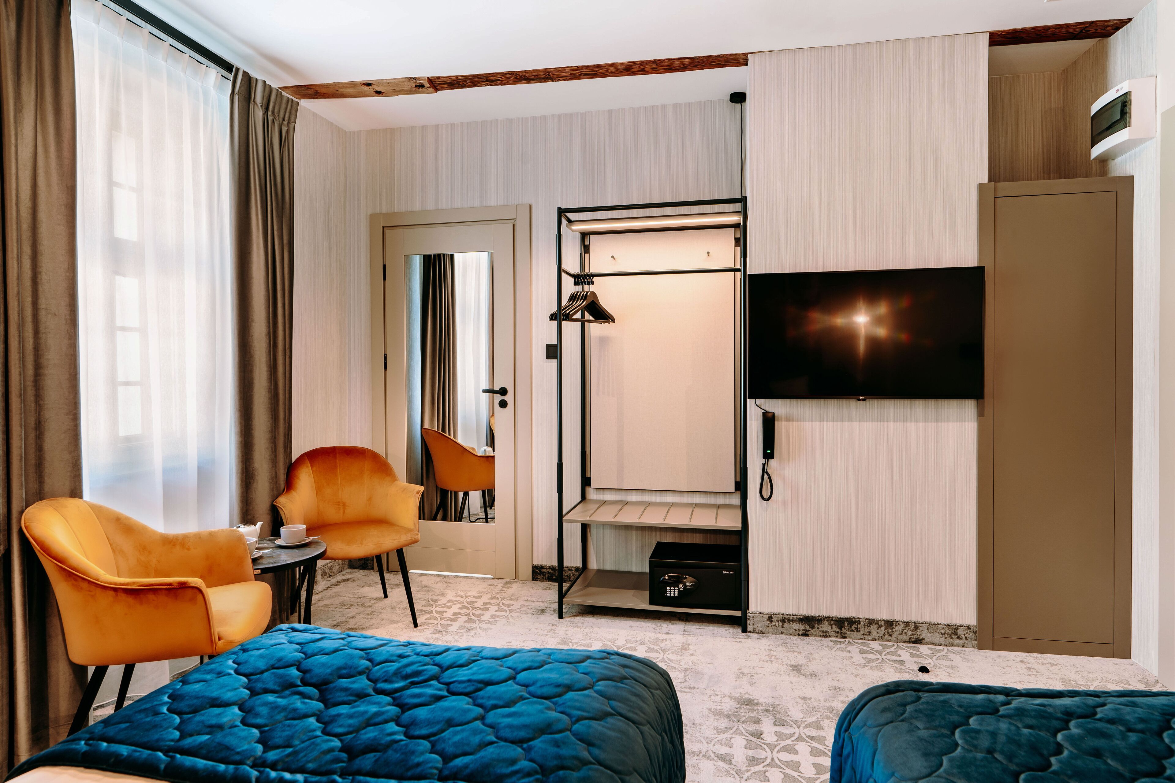 A hotel room with a bed, two chairs, a TV, a wardrobe, and a small table with a cup and saucer.