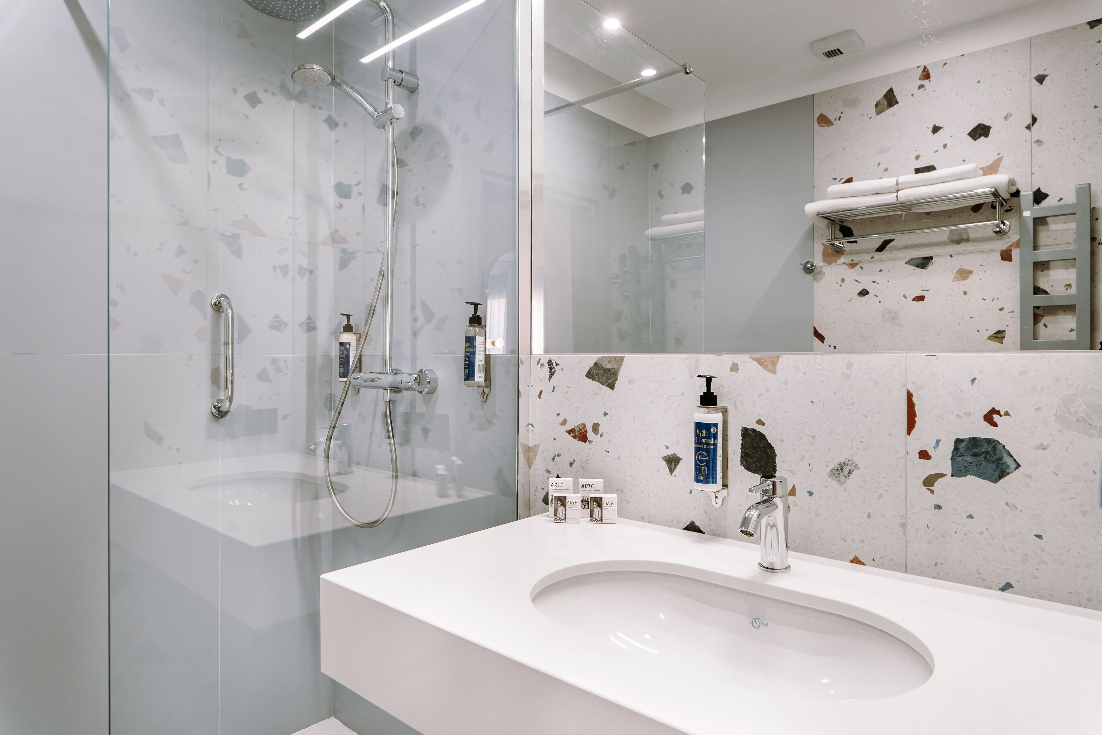A modern bathroom with a glass-enclosed shower, a white sink, and a terrazzo-patterned wall.