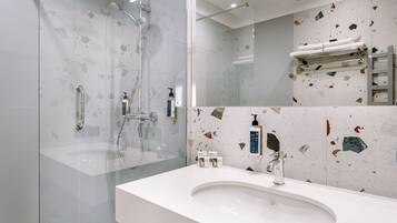 Un baño moderno con ducha de vidrio, un lavamanos blanco y un revestimiento de pared con estampado de terrazzo.