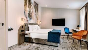 Ein Hotelzimmer mit einem Bett, einem Schreibtisch, einem Stuhl, einem Fernseher und einem großen, abstrakten Gemälde an der Wand.