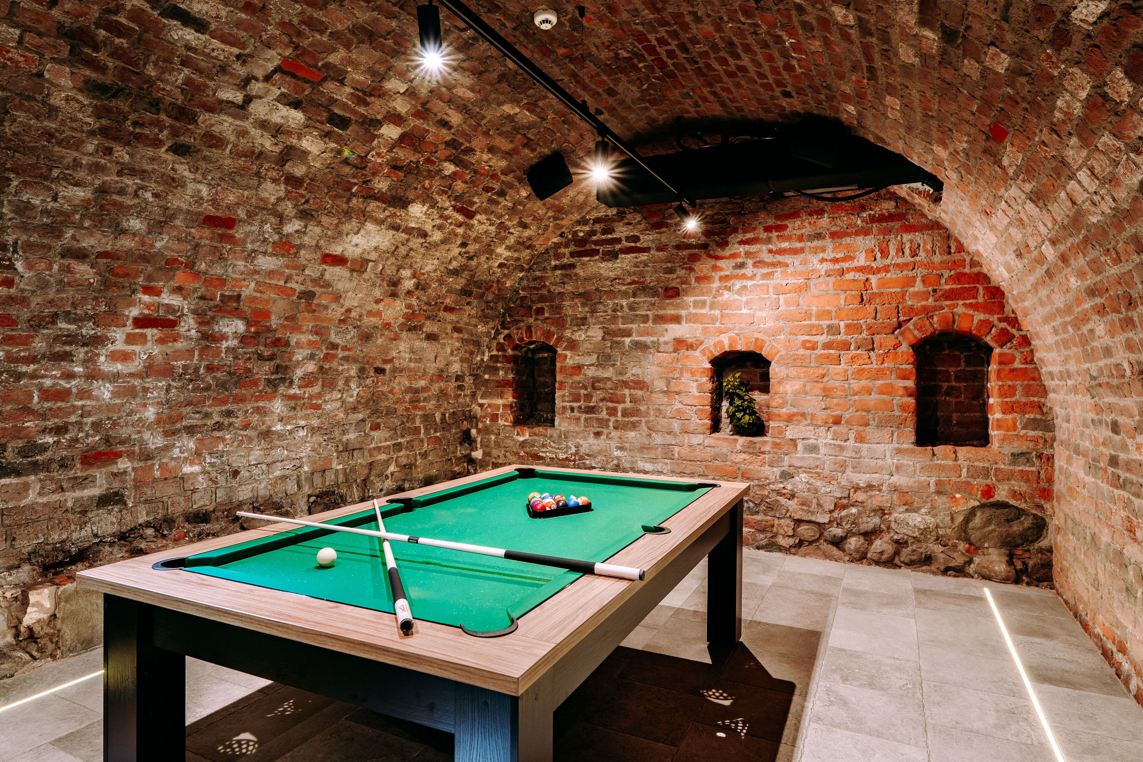 A pool table in a room with brick walls and arched windows.