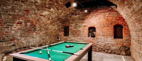 A pool table in a room with brick walls and arched windows.