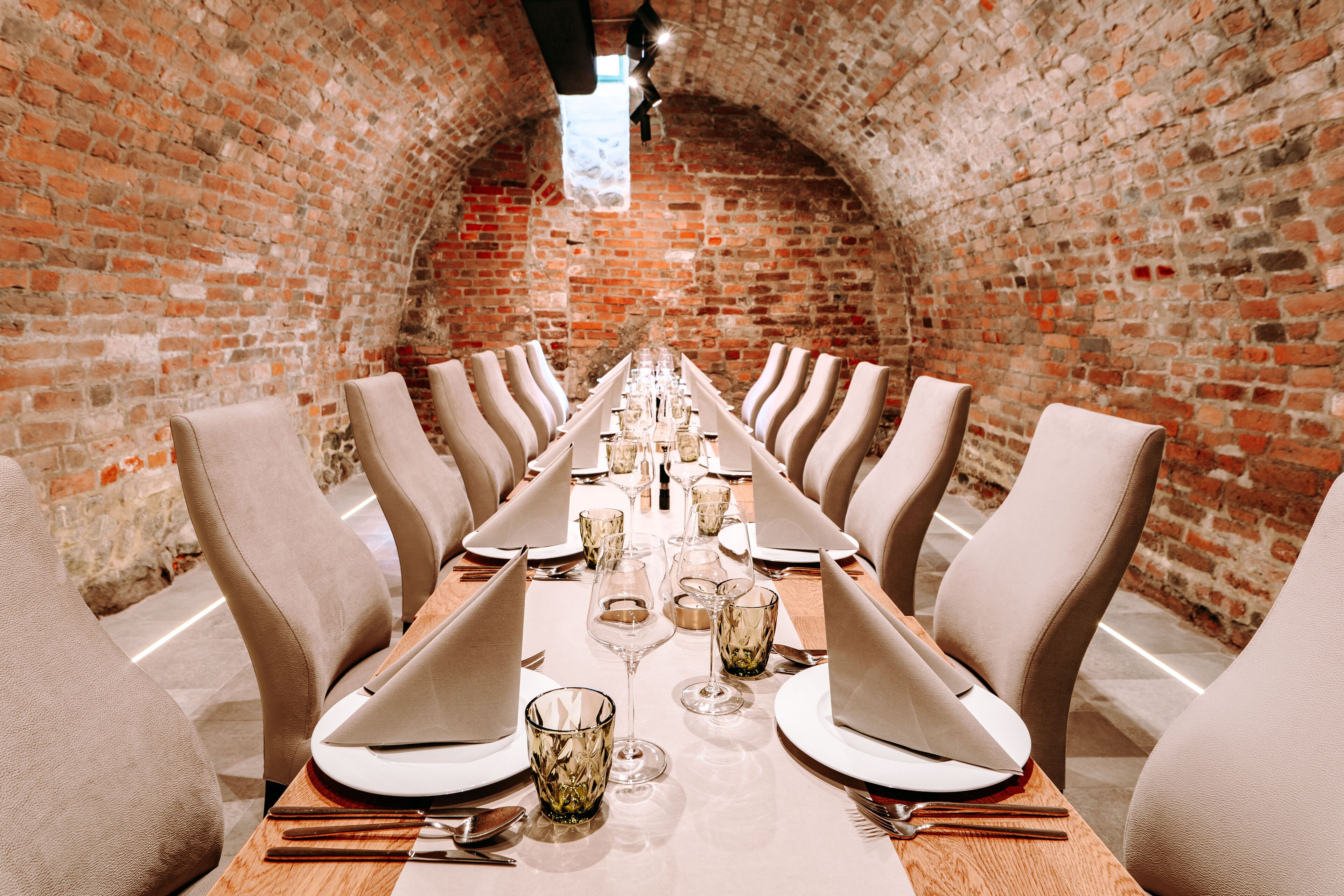 A long dining table set for a meal in a brick-walled room with high ceilings and arched brick arches.