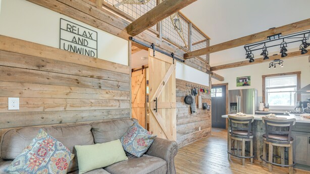 Ein gemütliches Blockhaushaus-Interieur mit Holzvertäfelung, einer Couch mit gemusterten Kissen und einer Küchenzeile mit Barhockern.