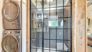 Ein modernes Badezimmer mit einer gläsernen Duschkabine, Holzboden und einem sichtbaren Waschbereich mit zwei Waschmaschinen.