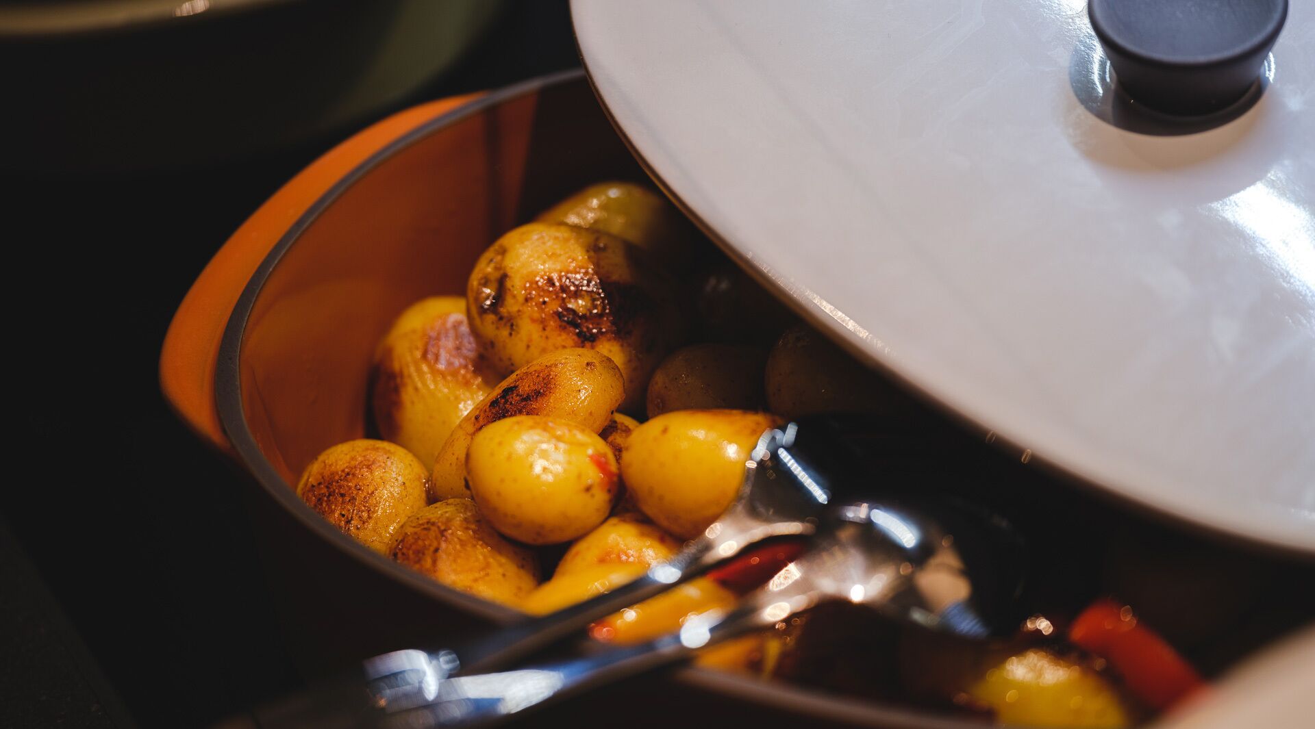 A close-up of a pot with roasted potatoes and a lid.