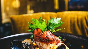 A seafood dish with mussels and a lobster tail, garnished with parsley, served on a black plate.