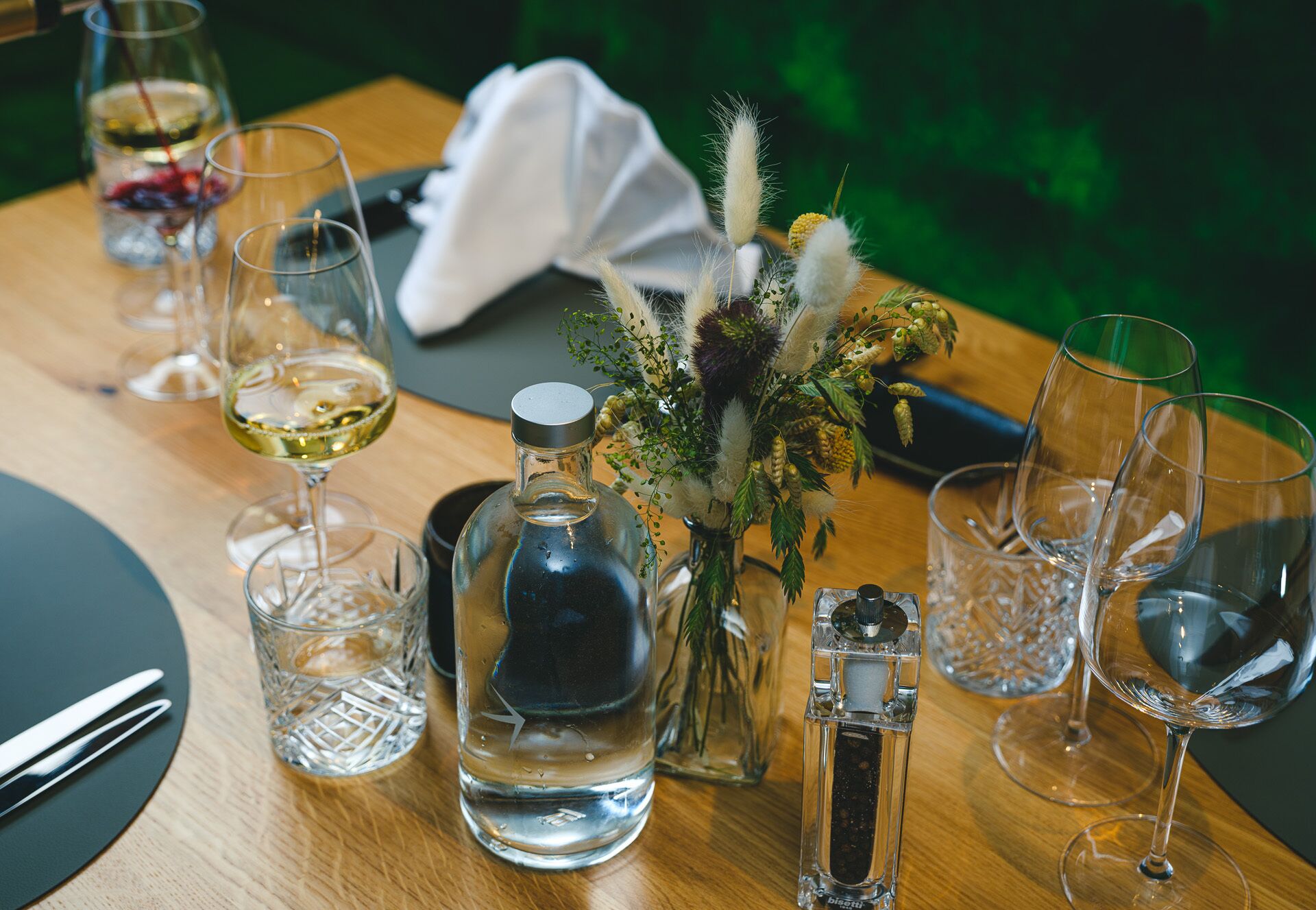Un tavolo da pranzo apparecchiato con bicchieri da vino, una bottiglia d'acqua e un centrotavola decorativo.