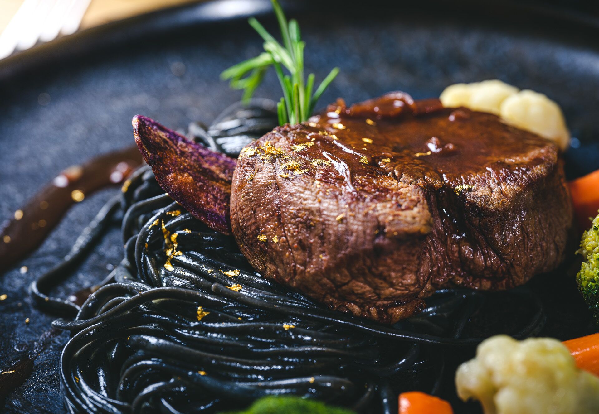 Een steak met donkere saus, gegarneerd met kruiden, geserveerd op een bord met groenten.