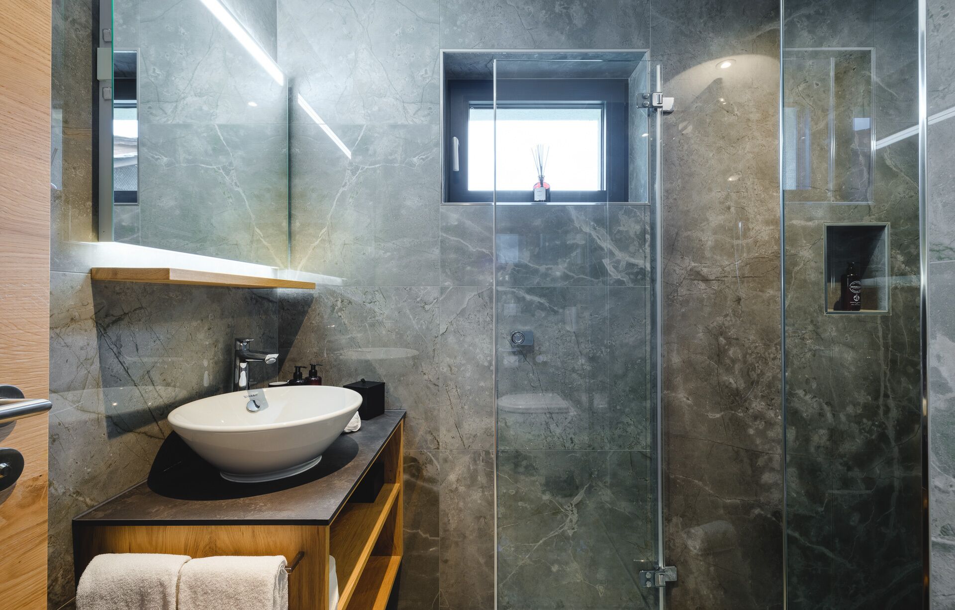 A modern bathroom with a large sink, a glass shower enclosure, and a small window.