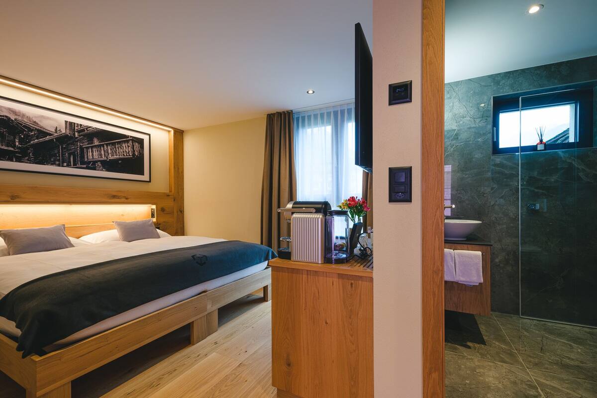 A modern hotel room with a wooden bed, a coffee machine, and a bathroom with a glass shower.
