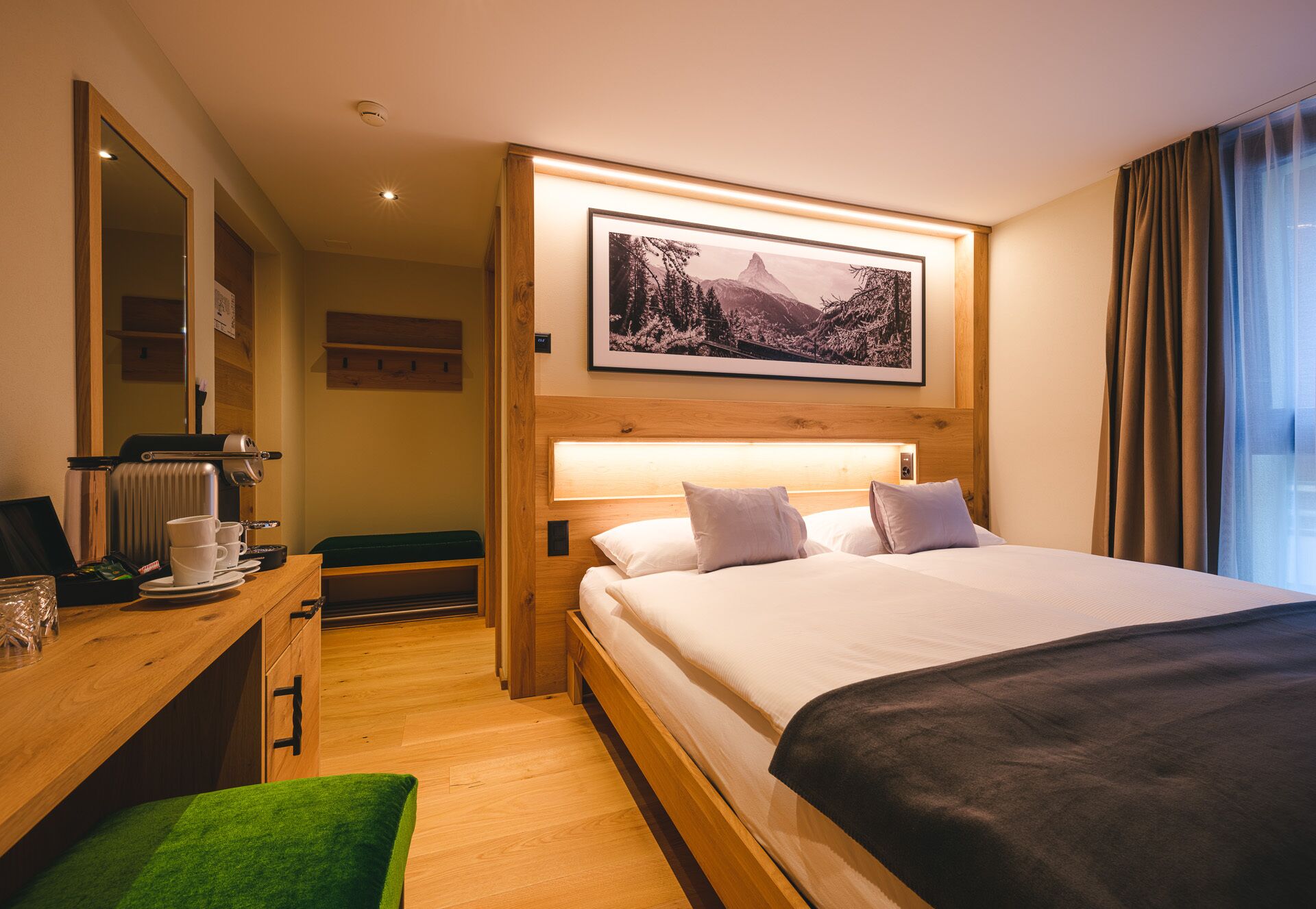 A hotel room with a bed, a desk with a coffee maker, a mirror, and a framed picture on the wall.