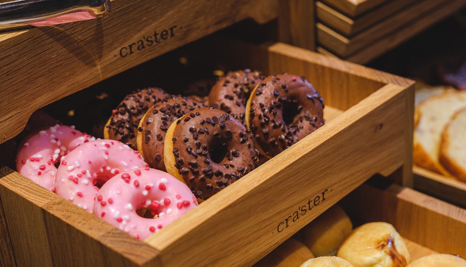 A wooden box containing various donuts, including pink frosted and chocolate-glazed varieties.