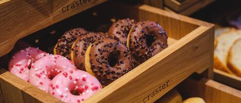 A wooden box containing various donuts, including pink frosted and chocolate-glazed varieties.