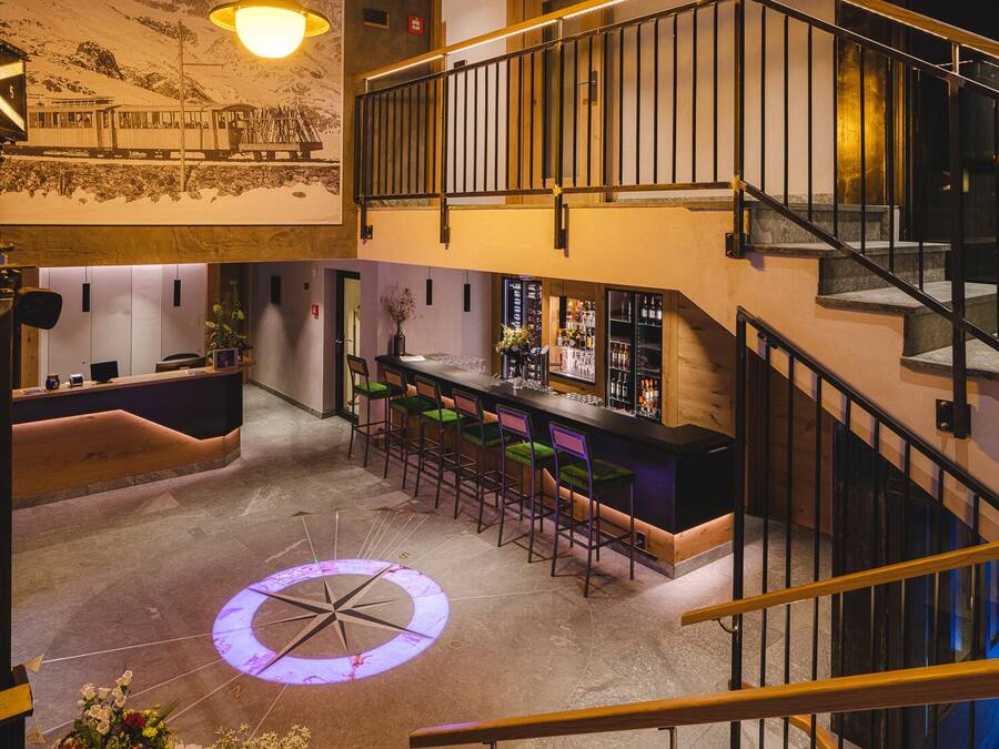 Un vestíbulo de hotel con zona de bar, una escalera y un gran diseño de brújula en el suelo.