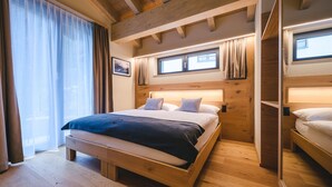 A wooden-framed bedroom with a large bed, a window with curtains, and a wooden ceiling. - Hotel Tannenhof (Zermatt)
