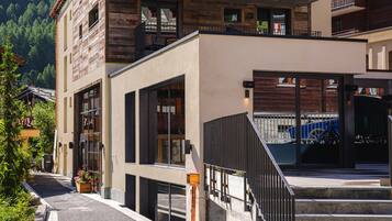 A multi-story building with a wooden facade and balconies, situated in a mountainous area with a clear sky.