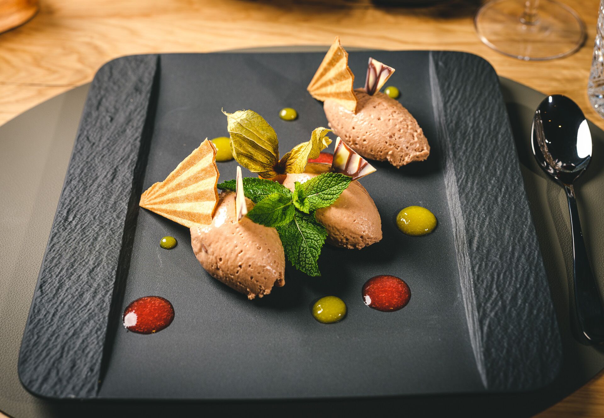 Un plato de postre con bolas de helado, hojas de menta y pedazos de oblea decorativa sobre una tabla de pizarra.