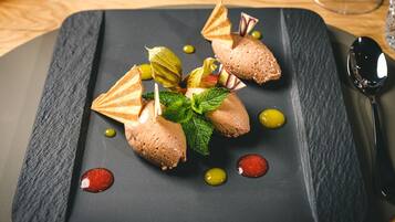 Un plato de postre con bolas de helado, hojas de menta y pedazos de oblea decorativa sobre una tabla de pizarra.