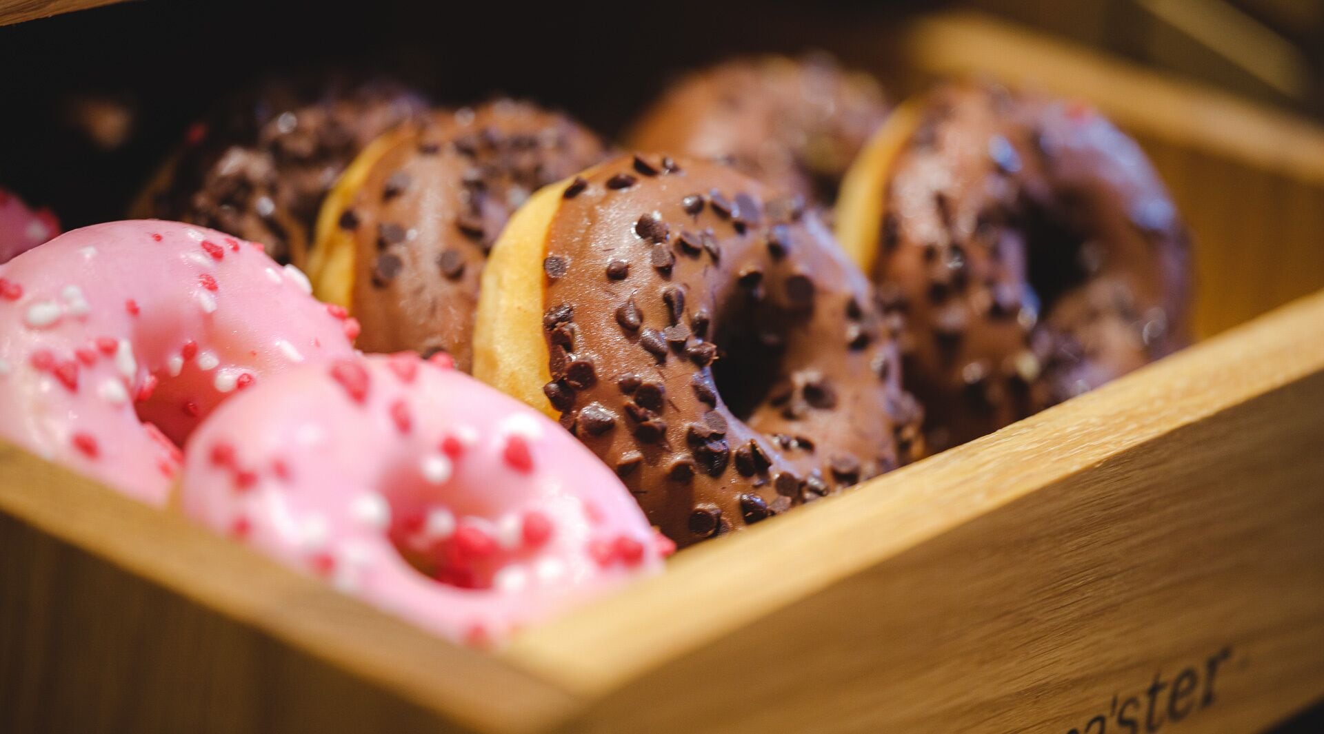 Een houten doos gevuld met verschillende donuts met uiteenlopende toppings.