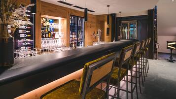 Una zona de bar con una barra alargada, varios taburetes y una amplia selección de botellas y vasos en estantes.