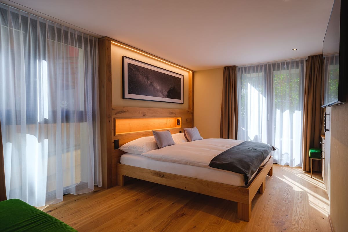 A modern bedroom with a wooden bed, sheer curtains, a mounted TV, and a framed picture on the wall.