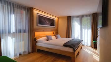 A modern bedroom with a wooden bed, sheer curtains, a mounted TV, and a framed picture on the wall.