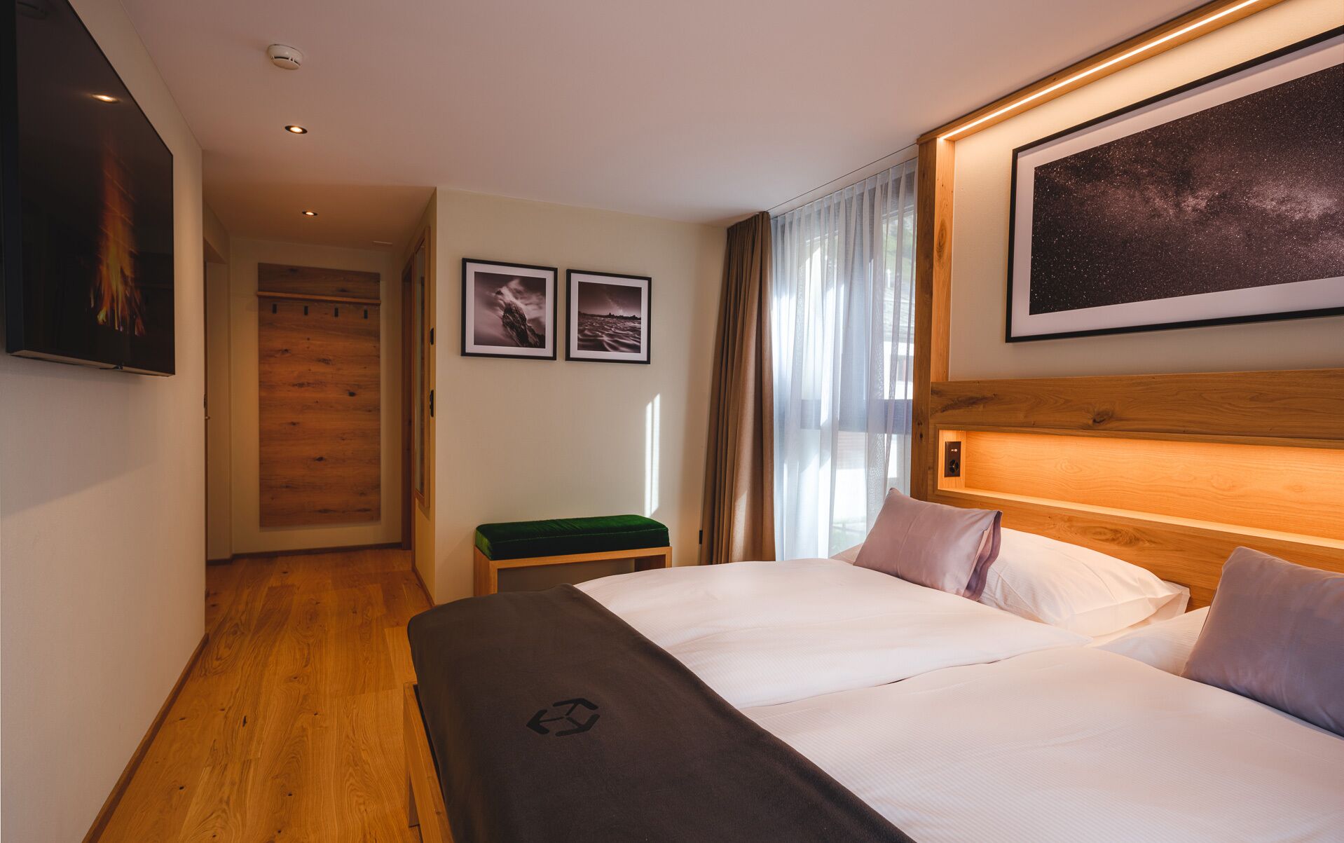 Habitación de hotel con una cama grande, cabecera de madera, un banco verde y dos cuadros en la pared.