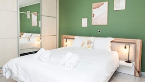 A neatly made bed with white linens and rolled towels, a bedside table with a lamp, and a mirror reflecting the room. - Elegant & Spacious  Apt. with Sea View (Piraeus)