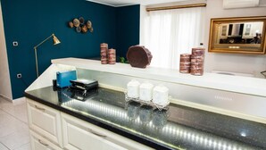 A kitchen with a black countertop, white cabinets, a blue appliance, and decorative items on the wall. - Elegant & Spacious  Apt. with Sea View (Piraeus)
