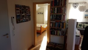 Un couloir étroit mène à une chambre à coucher où se trouvent un lit et une bibliothèque remplie de livres.