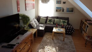 Un salon confortable avec un canapé, une télévision, des meubles en bois et une plante.