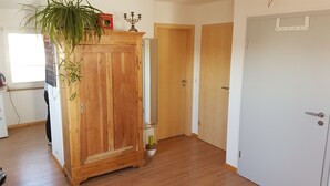 Une pièce avec un plancher en bois, une grande armoire en bois, une plante en pot et une porte dotée d’une poignée blanche.