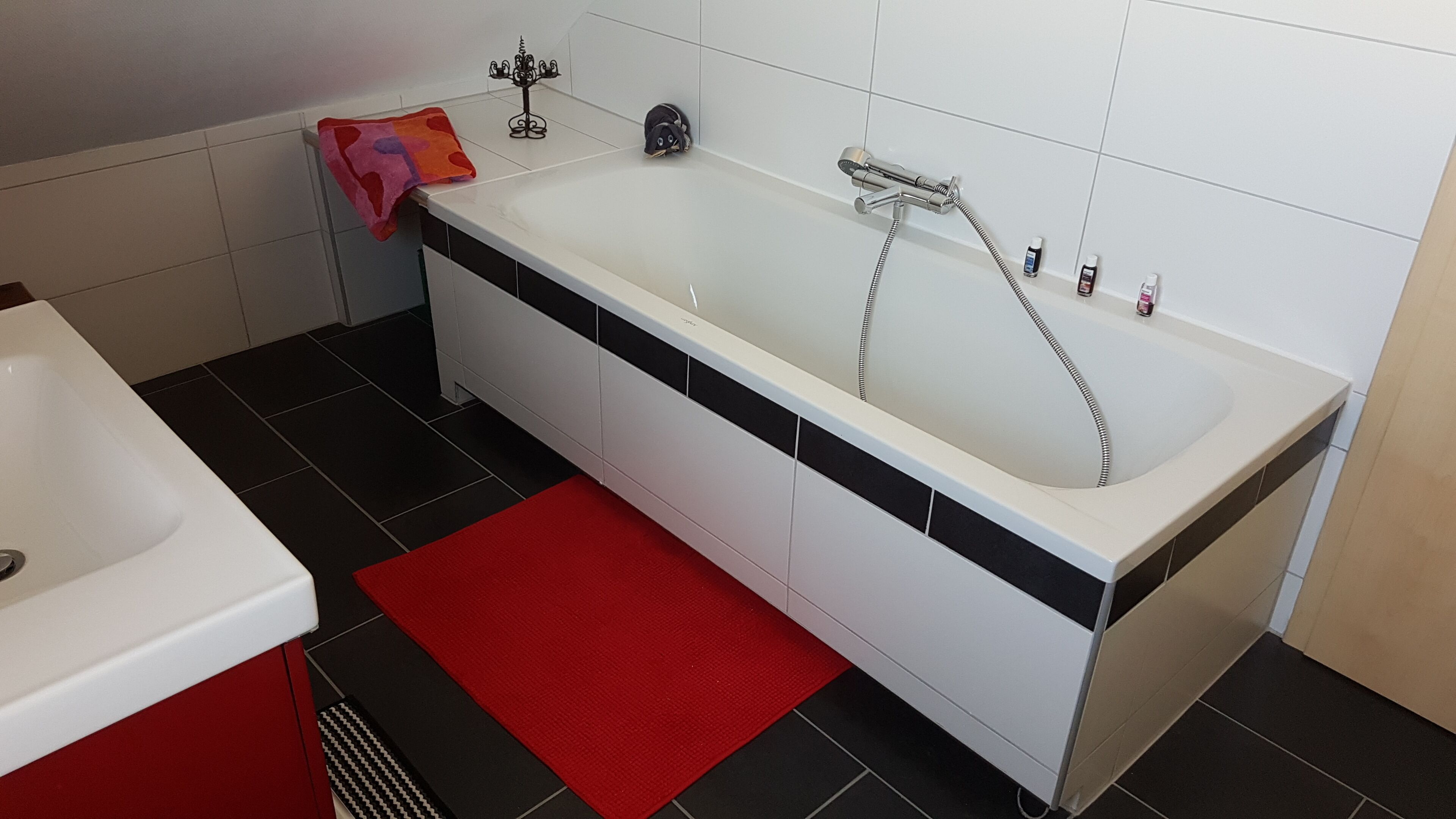 A modern bathroom with a white bathtub, black and white tiled walls, a red bath mat, and a black and white tiled floor.