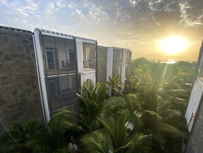 Un immeuble de grande hauteur offrant une vue sur le coucher du soleil, entouré d’une végétation luxuriante et de palmiers.