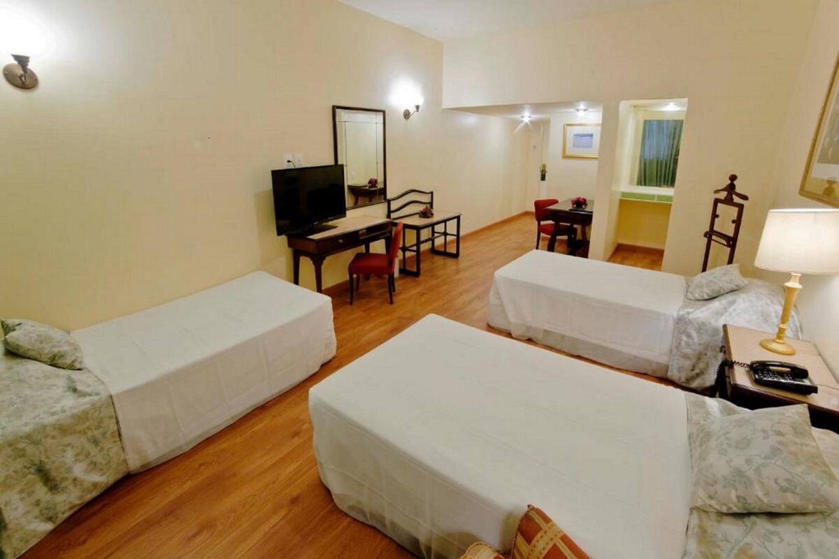Hotellihuone, jossa on kaksi erillistä sänkyä, työpöytä tuolilla, televisio ja pieni pöytä tuolilla.