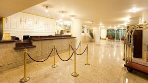 Un vestíbulo de hotel con una recepción, una escalera y un carrito de equipaje.