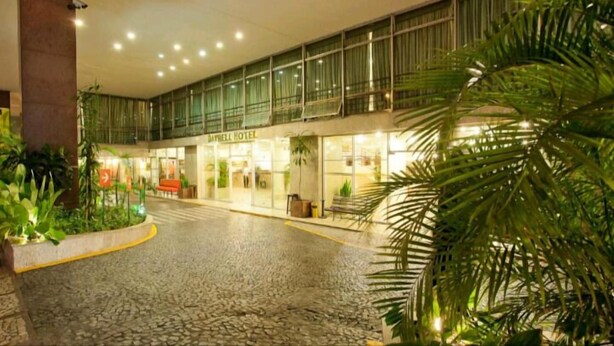 Entrada de un hotel con un porche cubierto, puertas de vidrio y plantas en macetas.