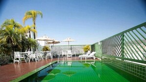 Una piscina en la azotea con baldosas verdes, sillas de descanso blancas y sombrillas.
