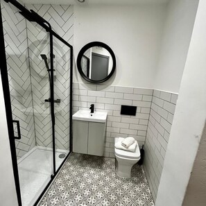 A bathroom with a shower, sink, toilet, and a mirror.