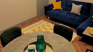 Ett vardagsrum med en blå soffa, en platt-TV, en målning av ett lejon och en kristallkrona.