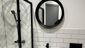 Ett modernt badrum med en duschavdelning med glasväggar, en vit tvättställ, en svart blandare, en rund spegel och en toalett med en handduk på.