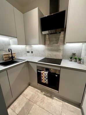 A modern kitchen with a built-in oven, a black range hood, and a stainless steel sink.