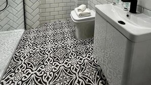 A bathroom with a herringbone tile pattern, a toilet, a sink with a black faucet, and a mirror with a herringbone tile border.